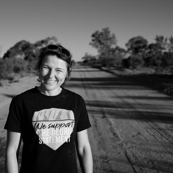 A woman standing on a dirt road, smiling at the camera