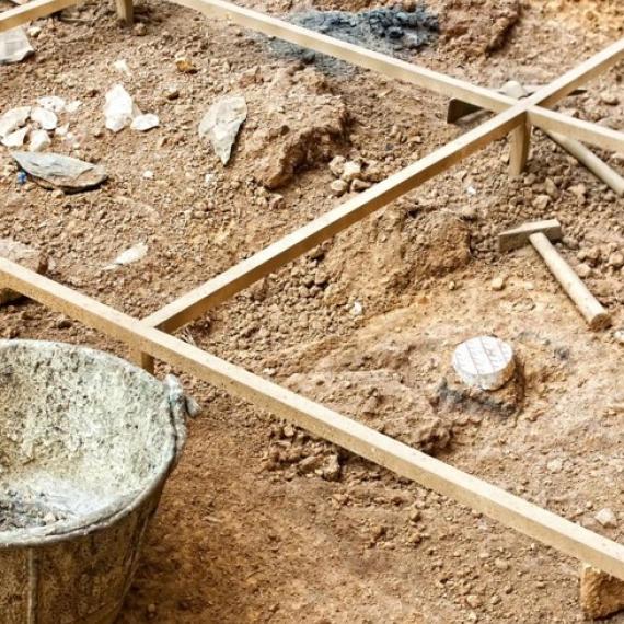 This image shows a close up section of an archaeological dig site. You can see a wooden grid demarcating the area and some tools. 