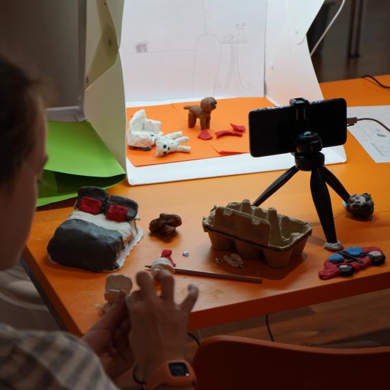 This shows a young person setting up a scene for their claymation animation before capturing it on camera.