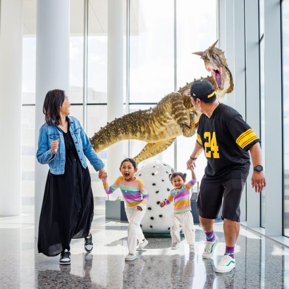 A family of four running away from a dinosaur exhibit in a Museum 