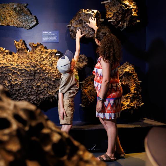 Woman and boy touch meteor inside Museum on the wall