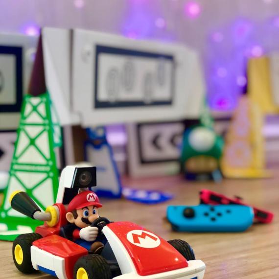 This is an image of the character Mario sitting in a red racing car . In the background are some hand controllers for the car.