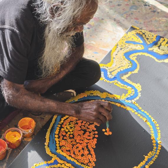 Aboriginal artist painting on the floor with bright colours