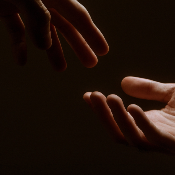 Two hands reaching towards each other against a dark background.