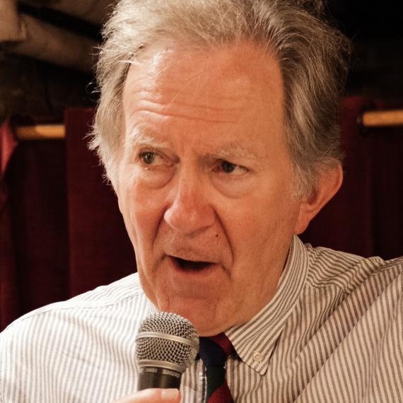 an adult wearing a white short and striped neck tie, holds a microphone and speaks with passion. 