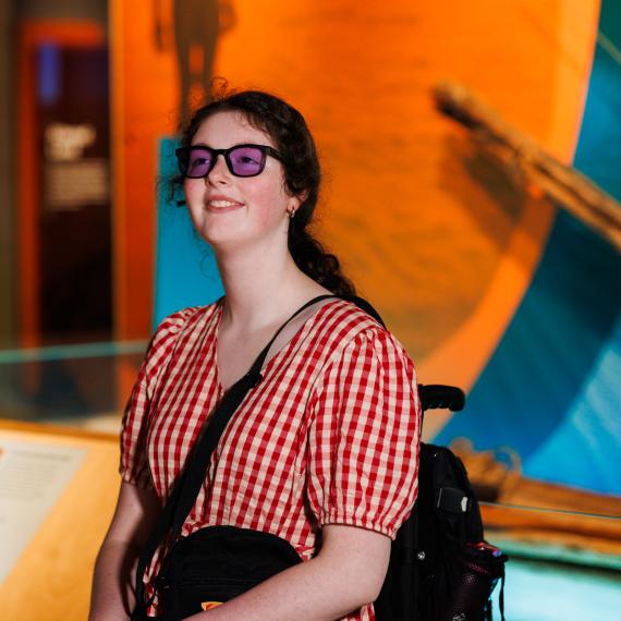 A smiling girl wearing colour blind glasses looking up in awe at a museum exhibit.