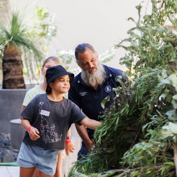 Image shows two peopl using branches to construct an Nyoongar shelter called a kalak. 