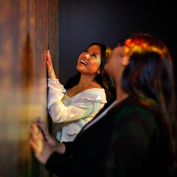 a group of adults are close to a wall of artwork and look up with a happy expression on their faces