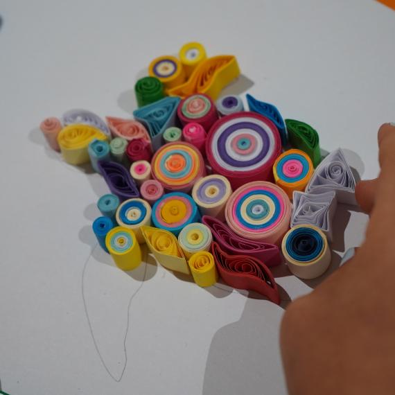 Quilling involves the rolling of strips of paper into shapes and then creating a piece of artwork with them. This images shows a piec eof artwork being created using many different colours and shapes of quills. 