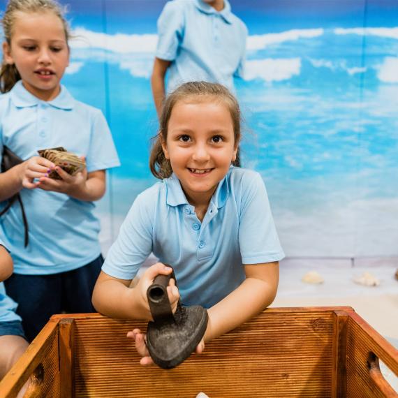 A girl student holds an antique iron during an education program session of Shipwrecked at WA Shipwrecks Museum