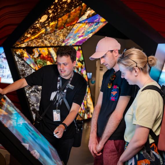 Two visitors on a tour with a staff member looking at a digital screen