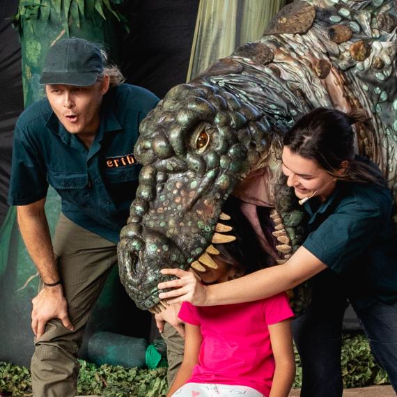 Giant dinosaur puppet towering over a little kid mid performance