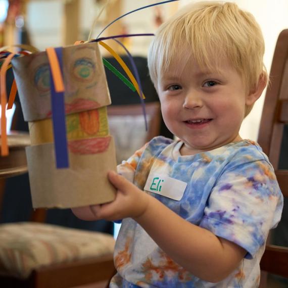 a young toddler smiles and holds up their cardboard puppet