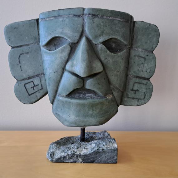 Stone sculpture of a stylized human face with geometric carvings, mounted on a base.