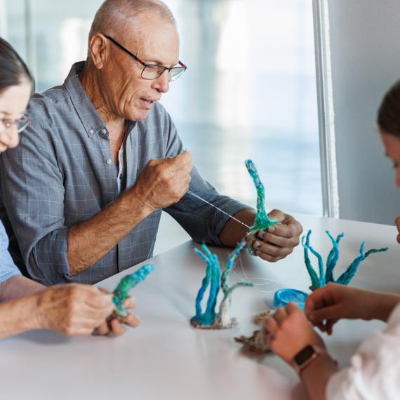 A small group are shown sewing ghost net materials into marine fauna project elements for a Maritime Crafternoon ghost nets art activity workshop.