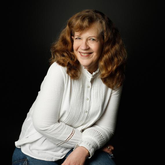 a headshot of a person with a warm smile. They wear a white top and jeans
