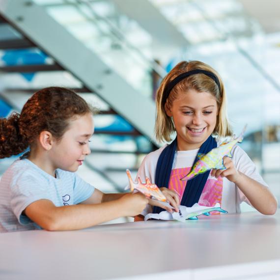 Two girls playing with sawfish finger puppet colouring at the WA Maritime Museum for July 2025 school holidays.