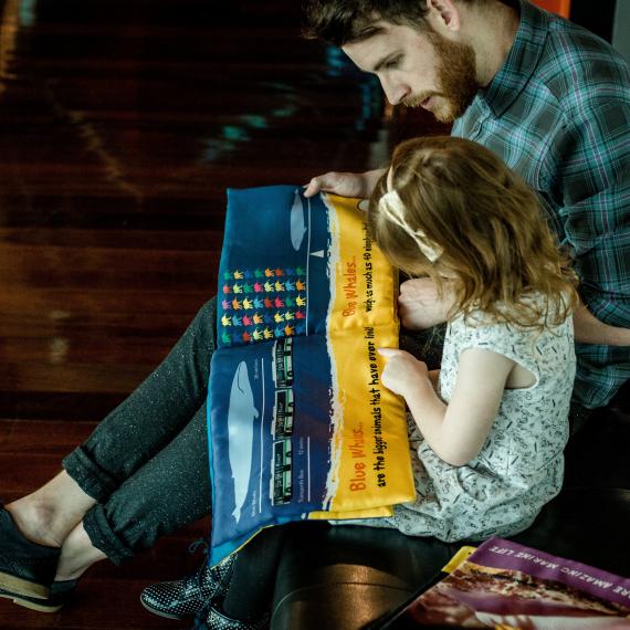 a young child and reads a sea story book with an adult next to them guiding them
