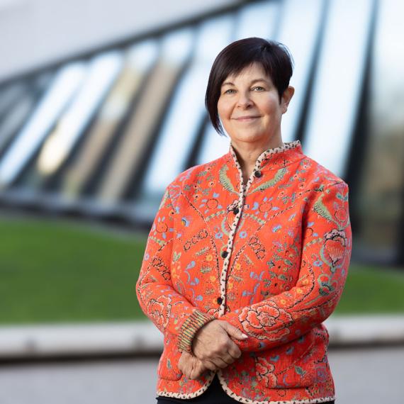 a person stands in front of a building with their arms crossed with a friendly smile