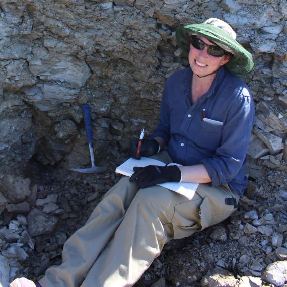 a person sits in a pit of rubble with picks and takes notes on her book.