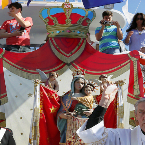 Priest, officials and festival goers on a boat being blessed on a sunny day