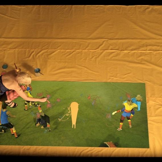 Artist painting on green paper on the floor with a variety of coloured paints and superimposed digital images of young people interacting on a sports field