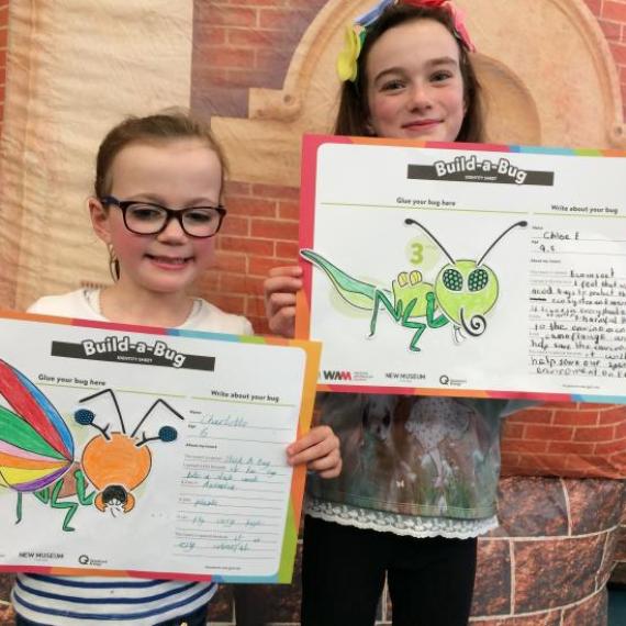 two children hold up their bugs they have crafted with paper 