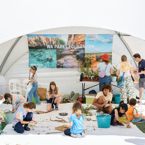 People engaged in outdoor activities under a white tent featuring a "WA Parks Foundation" banner.