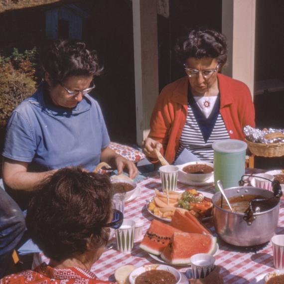 a photo of women around a dining table outdoors preparing food 