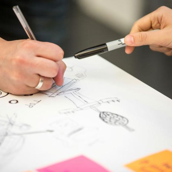 Image shows a close up of peoples hands as they sketch out their ideas on paper.