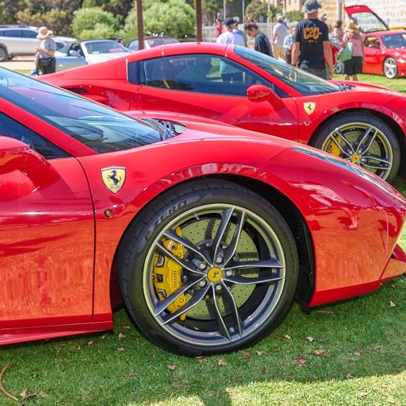 Two stunning bright red super cars showcased on a grassed area. There are people in the background admiring the cars. 