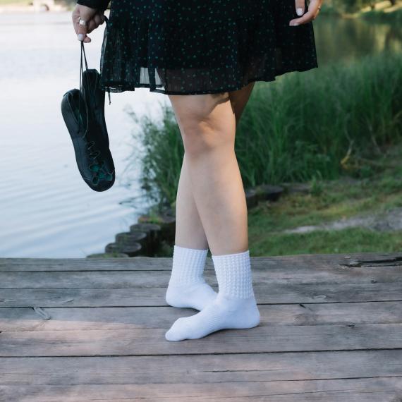 irish dancer pictured from waist down with feet crossed, holding dance shoes.  River and grass picture behind her. 