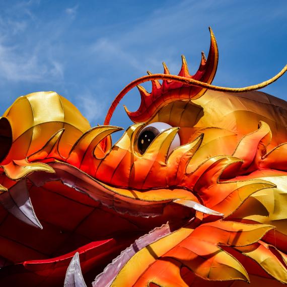 Bright red, orange and gold ornate dragon head with large nostrils and open mouth looking spectacular with blue sky behind it.  