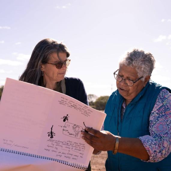 Two people look through a large folio standing in an outback area