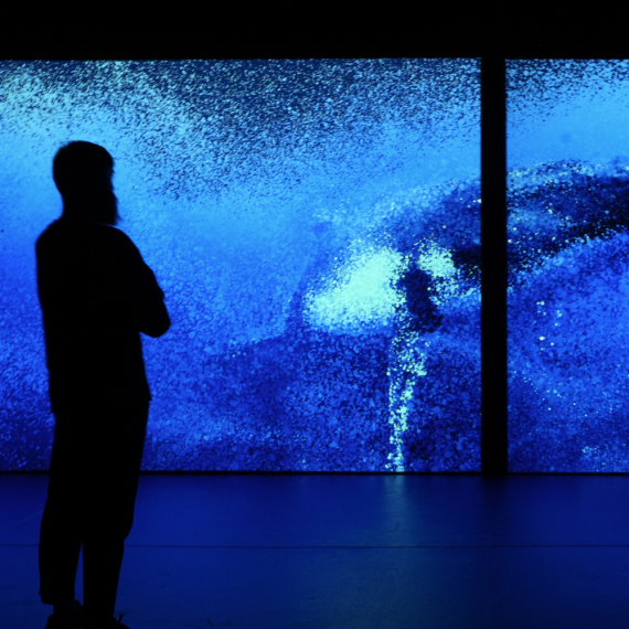 A person stands in silhouette before two large screens displaying a vivid blue underwater scene