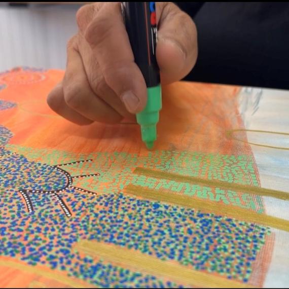 a close up of a colourful artwork and the artists hand adding to the work