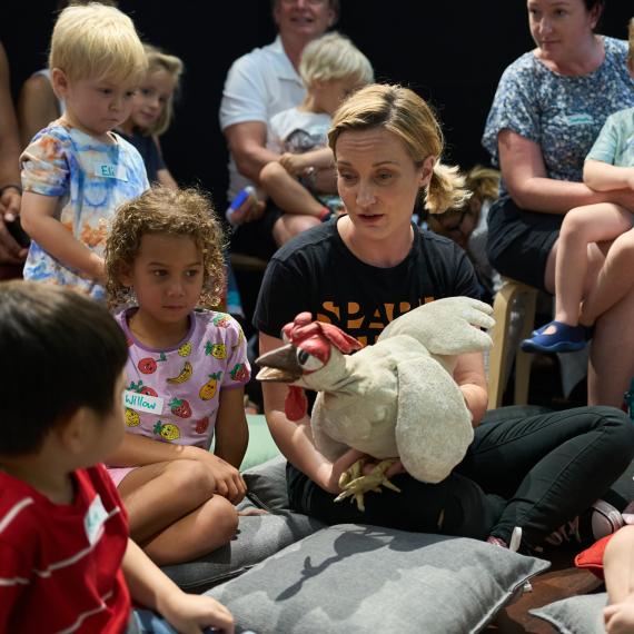 a group of children sit around an adult with a puppet 