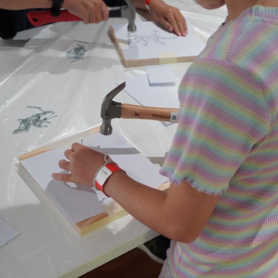 Kids hammering nails into picture template on pine board