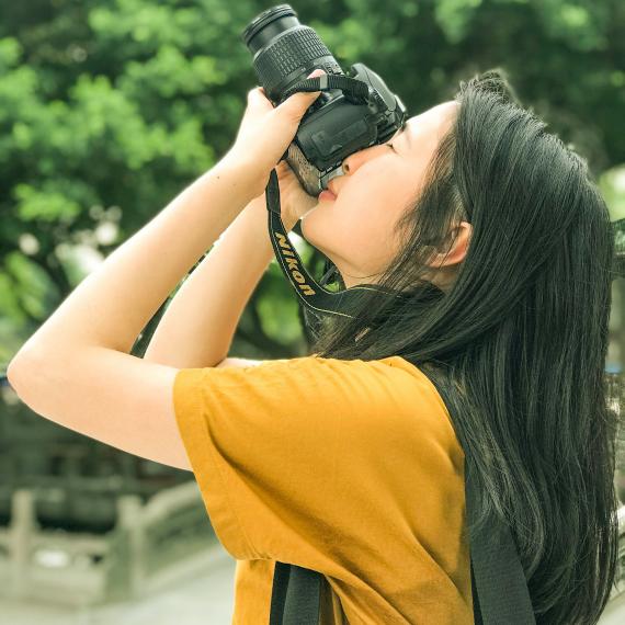 a person wearing a light coloured top looks up and aims to take a photograph with a camera