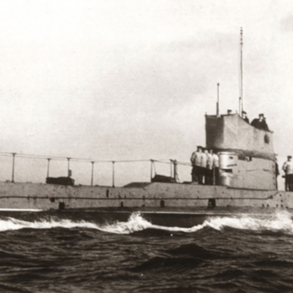 Black-and-white photo of a submarine marked “A52” travelling on rough seas, with crew standing on the deck.