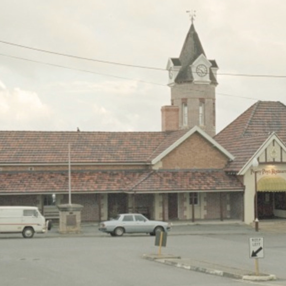 Street view of a historic railway station with a clock tower and parked cars in front.