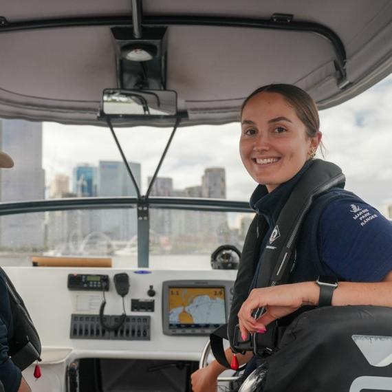 Two female Marine Rangers from WA's Department of Biodiversity, Conservation and Attractions shown at work on a patrol boat on the Swan River in front of the Perth city skyline.