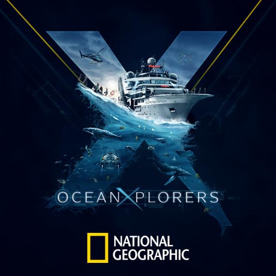 A large white research vessel, the OceanXplorer, sails across calm blue ocean waters with a helipad at the bow and multiple decks of scientific equipment, set against a clear sky and distant coastline.