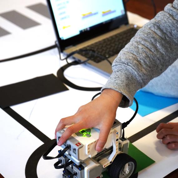 child's hand on EV3 robot with laptop in the background