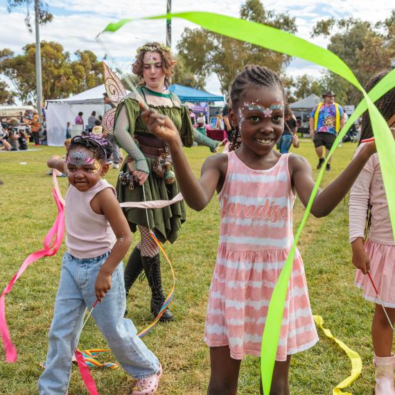 children playing outdoors in a park with streamers. They have their face painted and are having a great time smiling