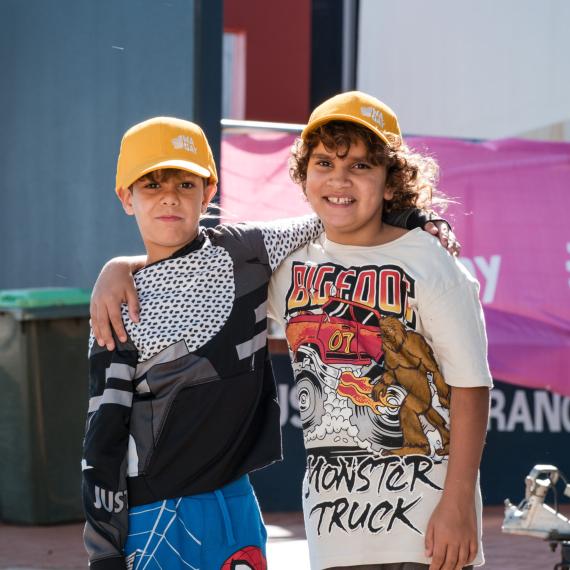 two children smiling and happy with yellow hats on and have one arm around eachothers shoulders 