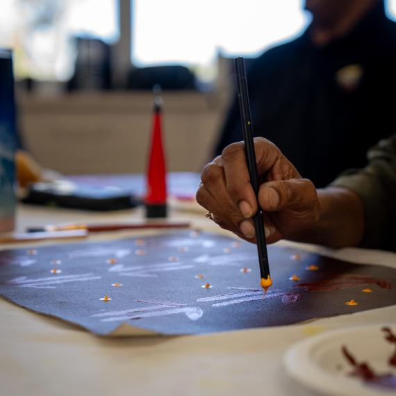 a close up of someone painting as they hold the painting tool dipped in yellow paint ready to apply to the paper