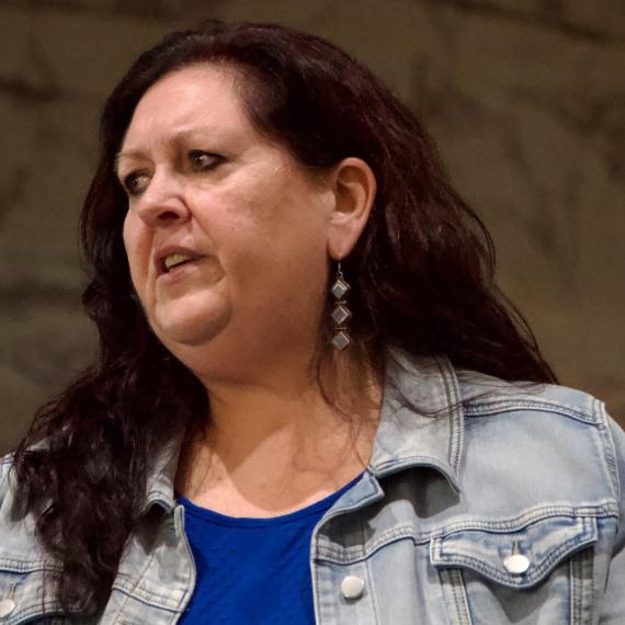 image of a person speaking. They are looking to the side as they are speaking and wear semi casual clothing