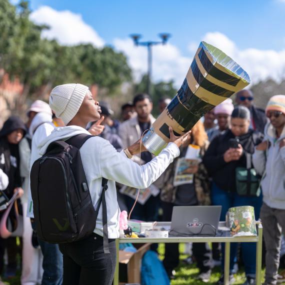 a crowd of people outdoors wher one person holds a tabletop telescope