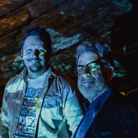 Filmmaker Brendan Hutchens and musician Lucky Oceans lit by ocean video projection onto the hull timbers of the Batavia in WA Shipwrecks Museum for the Tides music event (Fremantle Festival - 10 Nights in Port 2026).